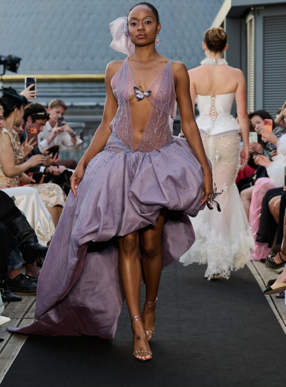 Mannequin défilant en robe violette ornée d'un papillon, maquillage lilas