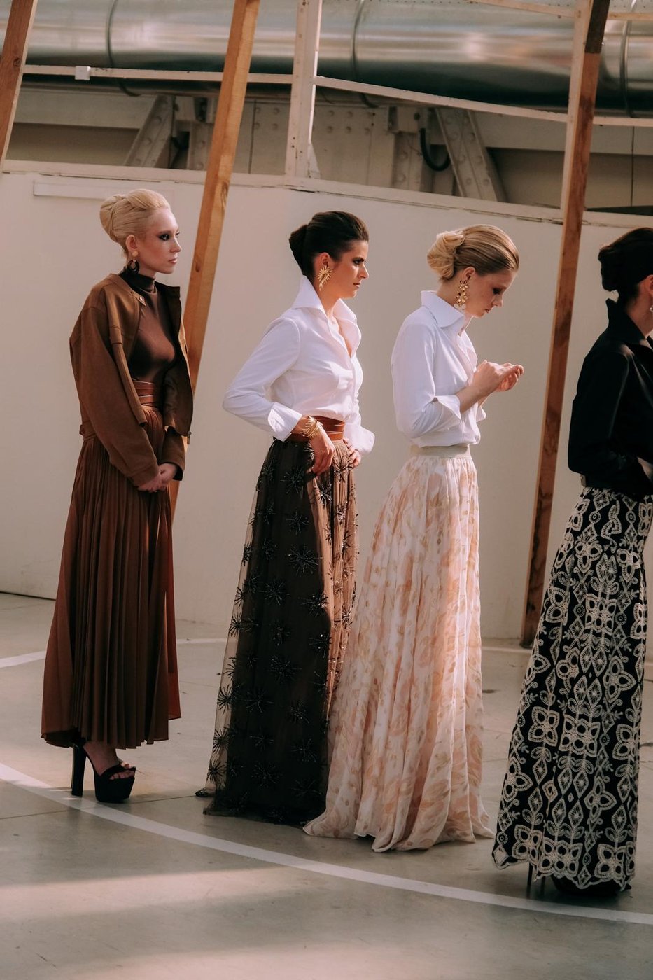 Coulisses d'un défilé : mannequins en jupes longues et chignons structurés