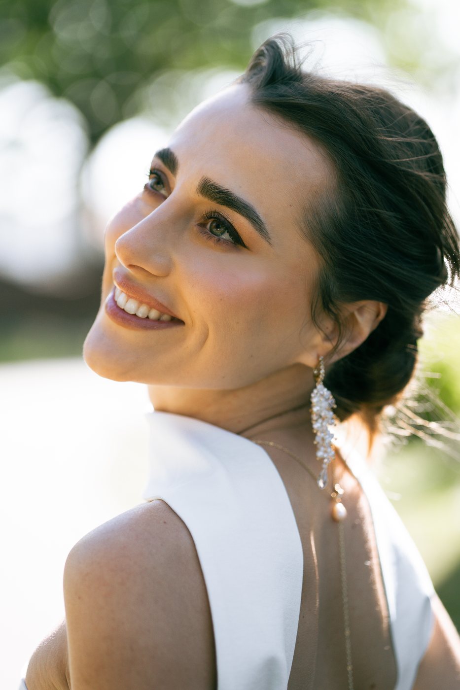 Portrait de mariée souriante en extérieur, teint lumineux et regard souligné