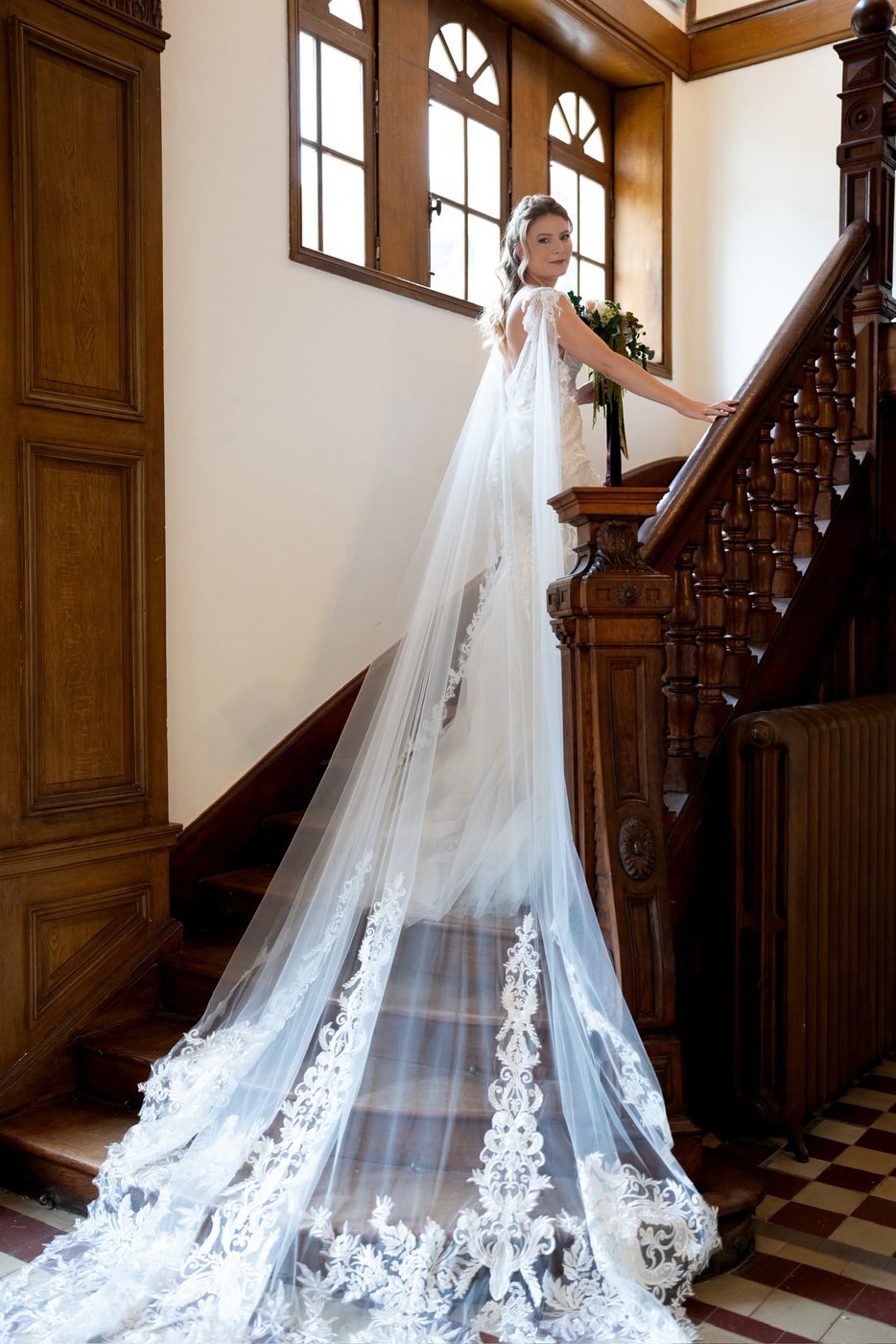Mariée en cape de dentelle sur l'escalier d'un château