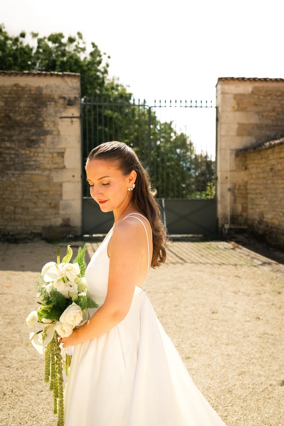 Mariée au bouquet blanc devant un portail de château en Vendée, maquillage naturel