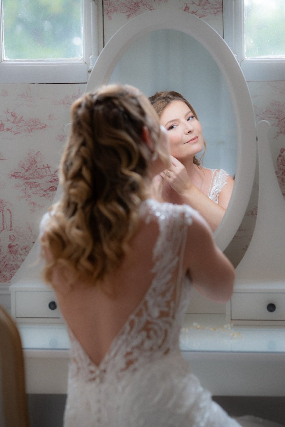 Mariée devant un miroir, coiffure bouclée et robe dos nu en dentelle